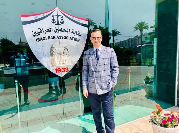 Haider Semaisim standing in front of the Iraqi Bar Association. He is wearing a plaid suit.