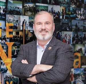 Roland Wilson in front of Mason Korea Collage, smiling with arms crossed.