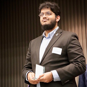 A man in a dark suit and glasses holds a glass trophy on a stage.