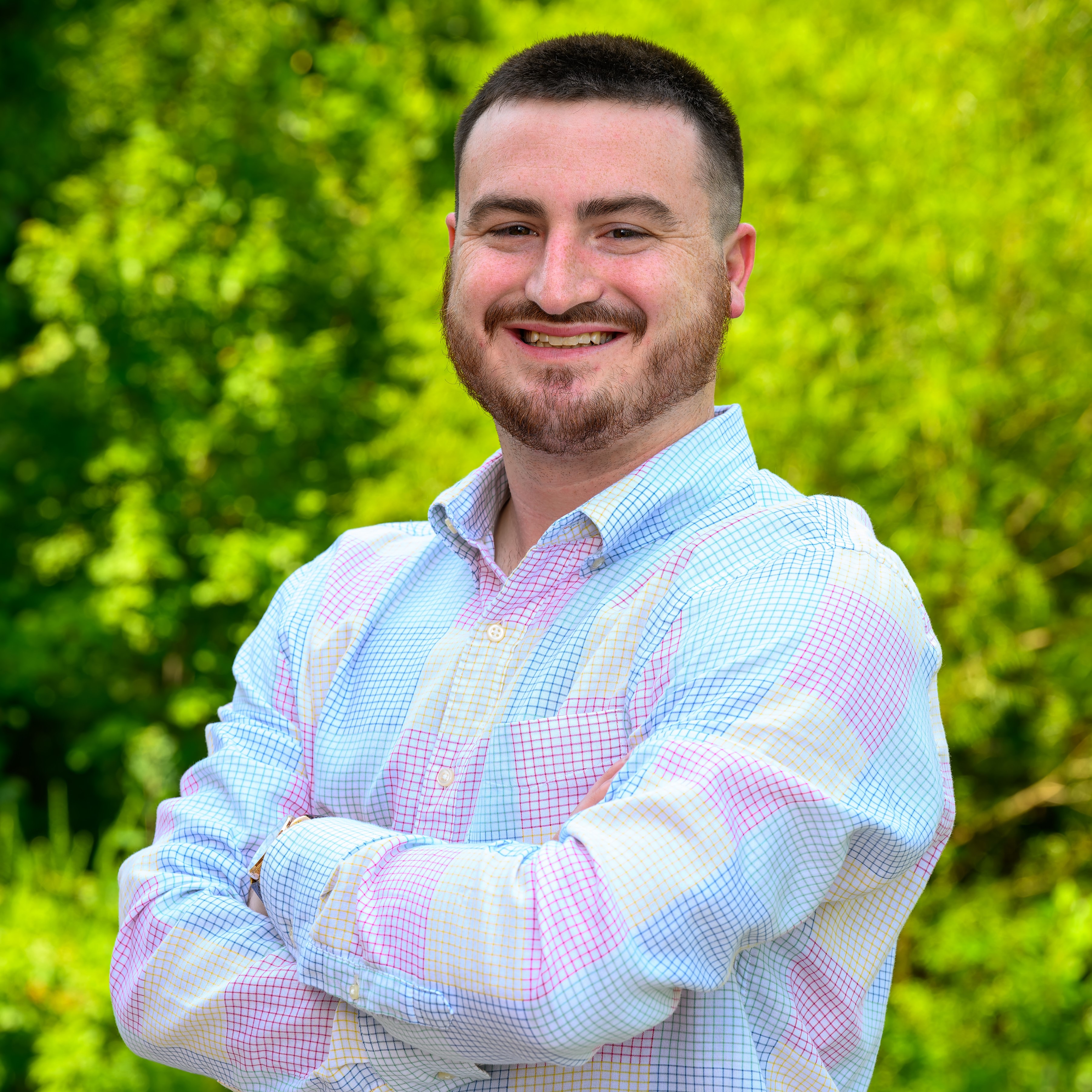 Jackson Pickard in a blue and pink collared shirt smiling with arms crossed