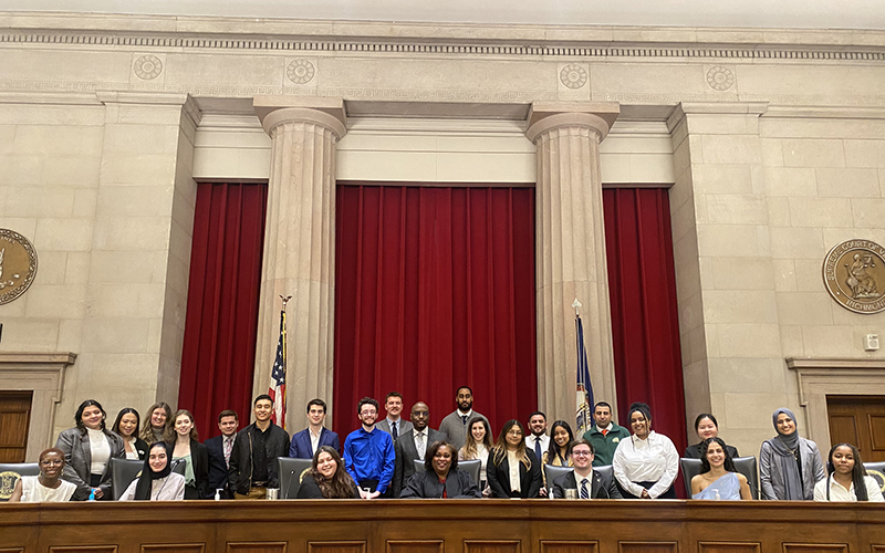 A group of students congregates around the bench and in front of two stone columns at the Supreme Court of Virginia. 