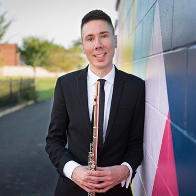 headshot of Prof. TJ Wible holding flute against a mural 