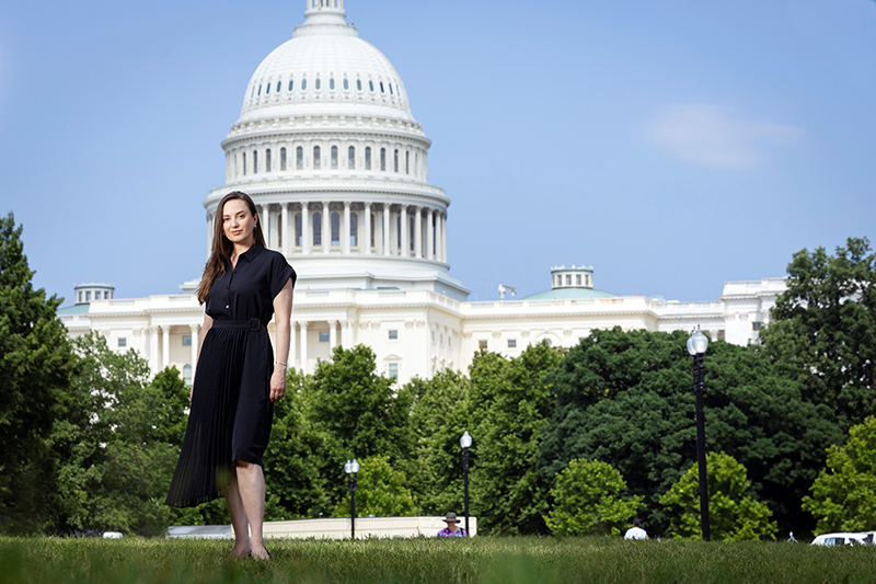 A woman in a dark top stands in front of the Capitol building.