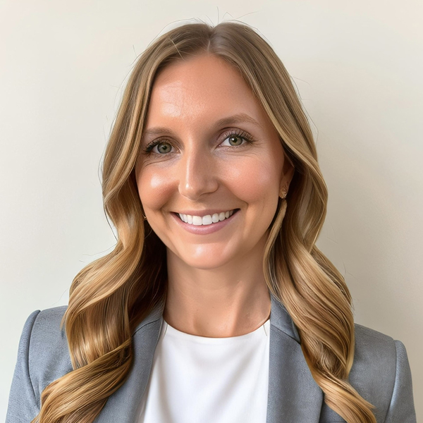 Shea M. Holman Kilian stands inside smiling while wearing a gray jacket and white shirt