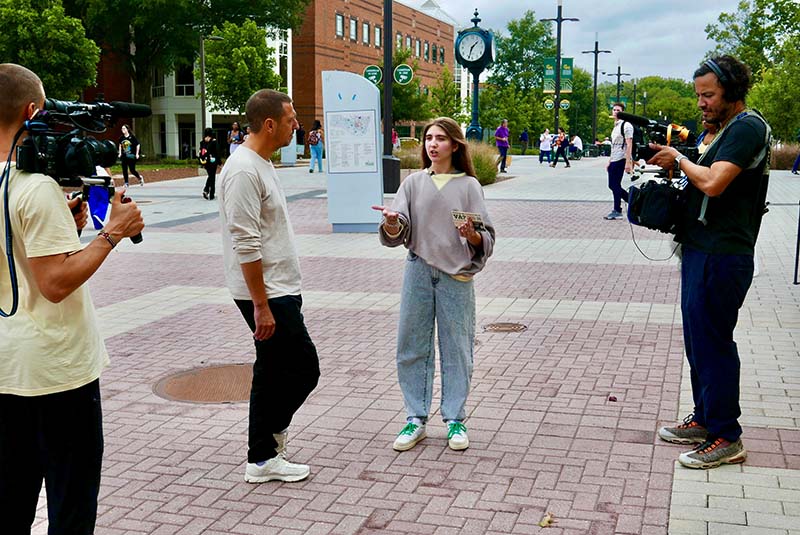 Three men and a woman stand in a plaza as the woman speaks.