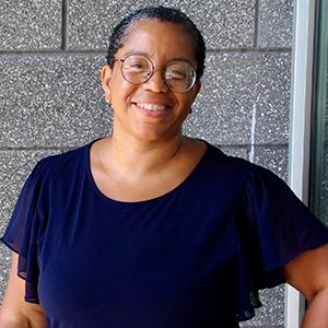 Thema Monroe-White stands outside while wearing a blue shirt and smiling