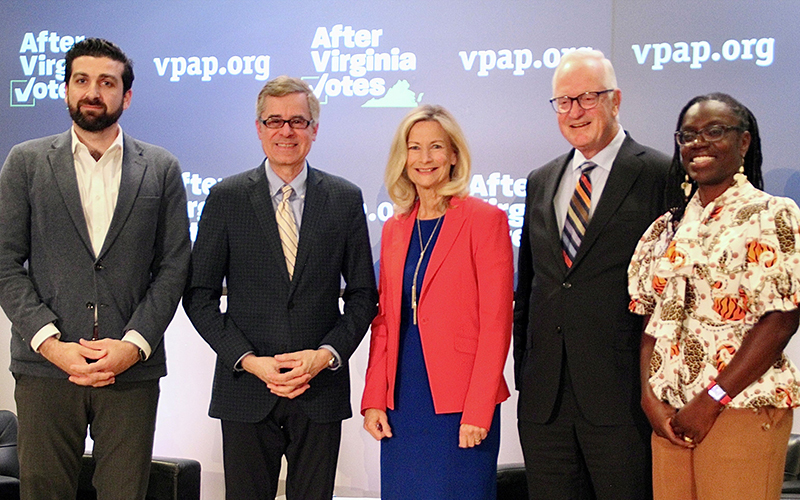 Five people, three men in suit jackets, and two women, one in a red jacket and the other in a printed blouse, smile at the camera.