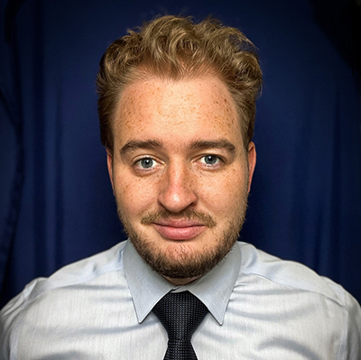 Brendan Sweeney wearing dress shirt with black tie against blue background