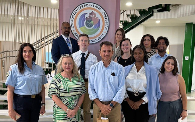 A group of people smile at the camera as they stand in front of a government logo.