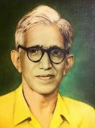 A man with round glasses and in a yellow shirt looks at the camera.