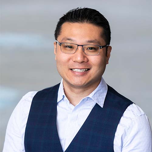 A headshot of CS assistant professor Wing Lam, wearing a light blue collared shirt and a navy blue vest.