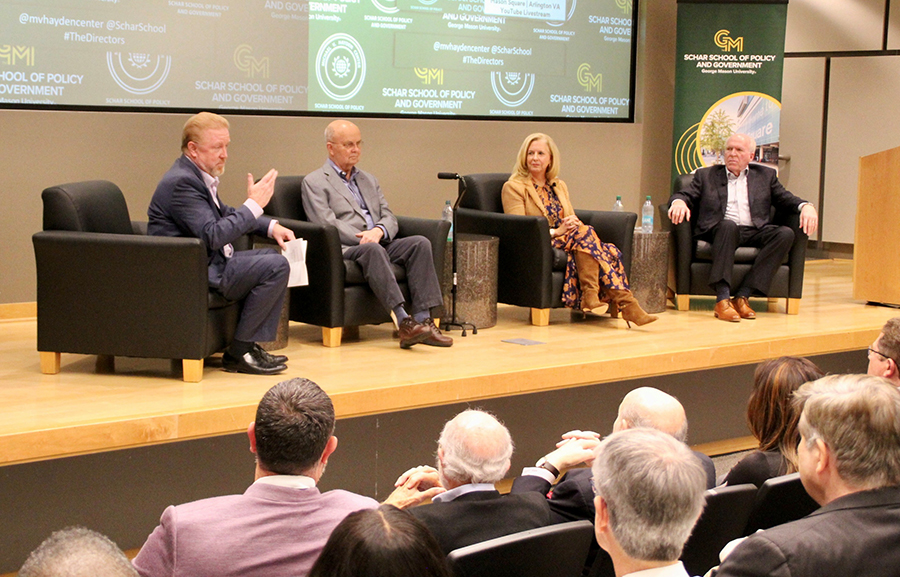 Four people sit in black chairs on a stage.