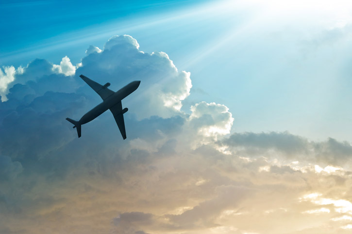 An airplane flies through partly cloudy skies