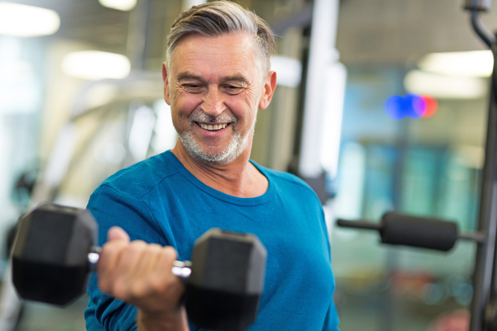 Grey haired man in gym lifting free weights