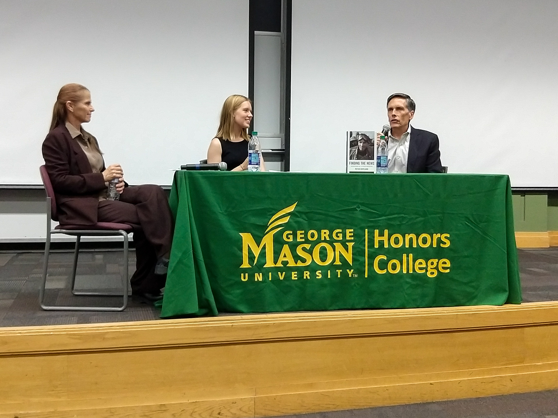 Zofia Burr, Sophia Chapin and Peter Copeland at an desk on stage with and Honors College banner on it