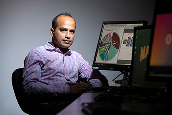 Huzefa Rangwala sitting at a desk with graphs on the screen. 