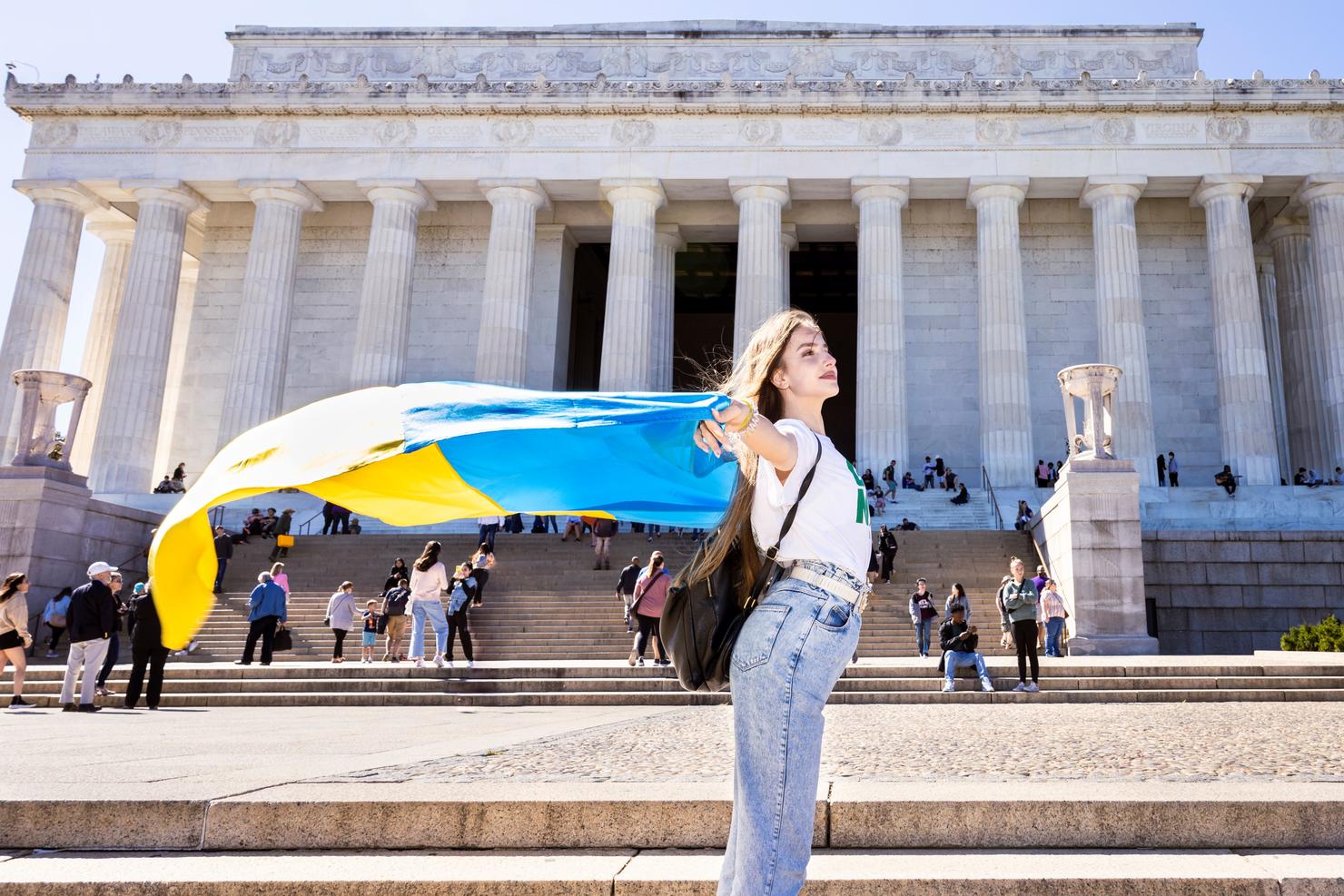 Mason student stands in front of the Lincoln Memorial while holding a Ukrainian flag flying in the wind over her head