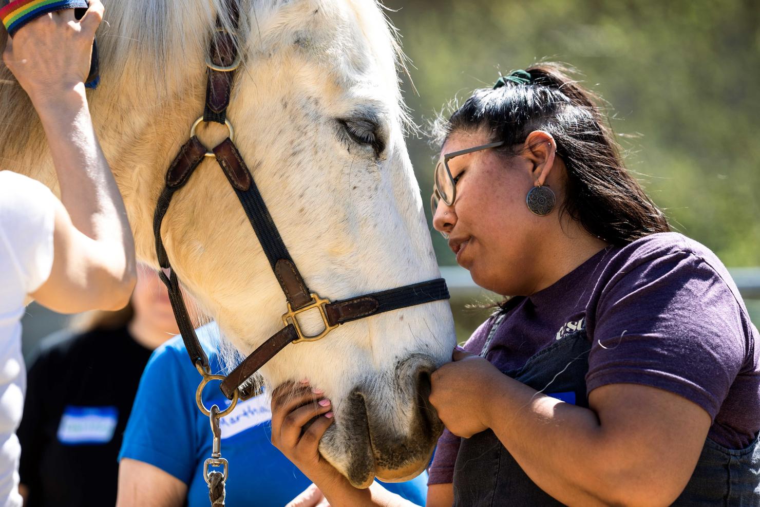 Mason social work student stands face to face with a horse from the Project Horse Empowerment Center, tenderly petting the horse's chin.