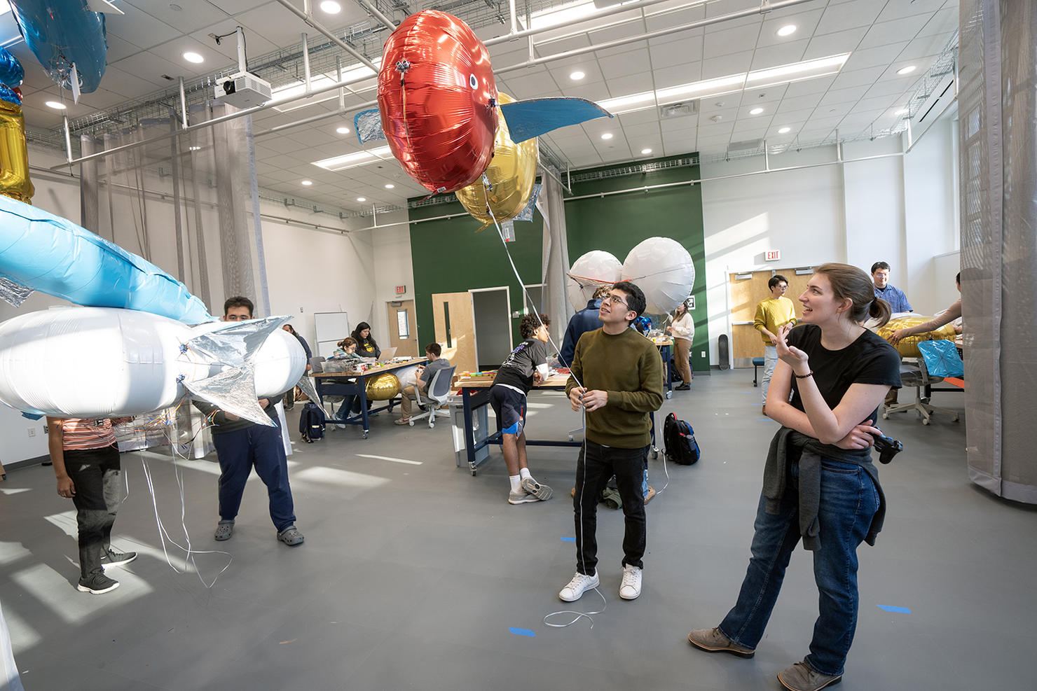 Students test their constructed blimps in a large, open industrial lab space, made of colorful mylar film.