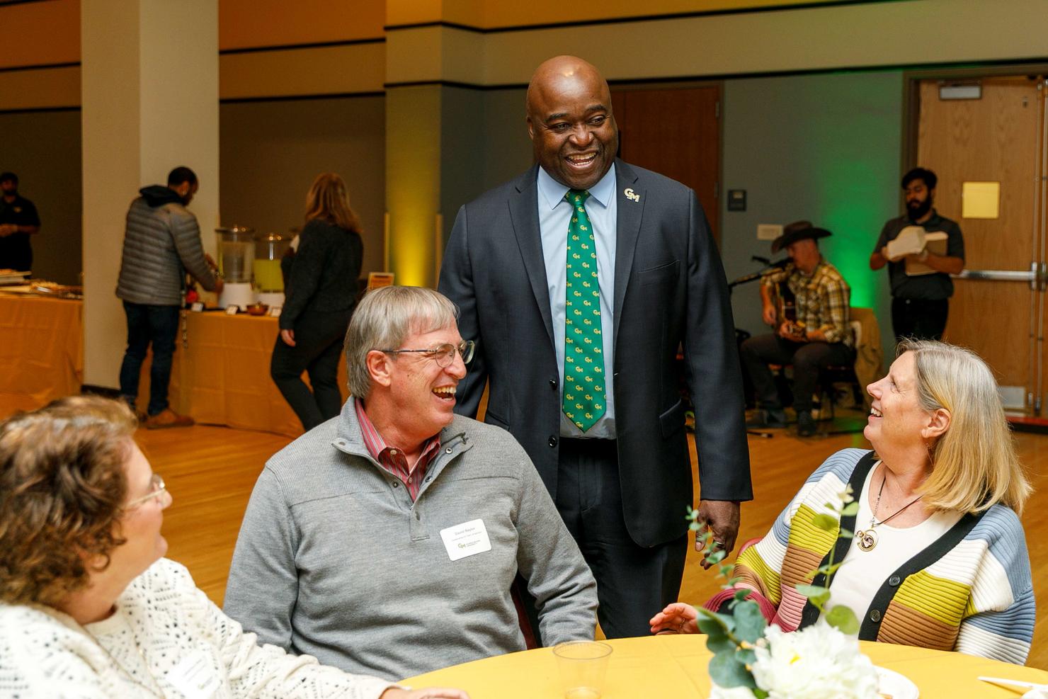 President Gregory Washington greets faculty and staff seated at a table during Gold Day luncheon