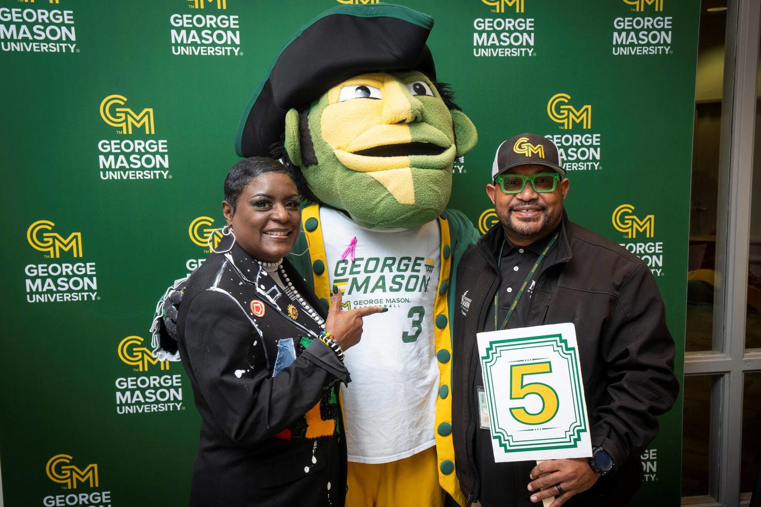 George Mason employees hold a sign that says 5 and pose with the Patriot mascot