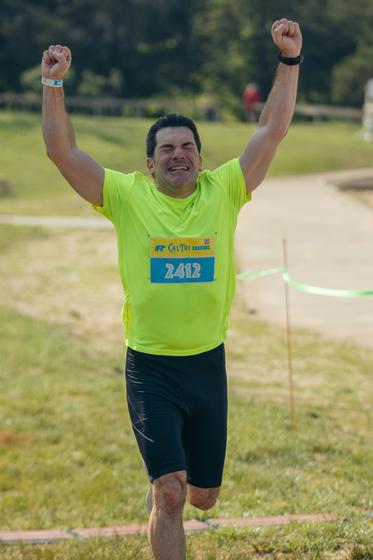 Kenneth Strazzeri crosses the finish line in a running race with his hands up in the air