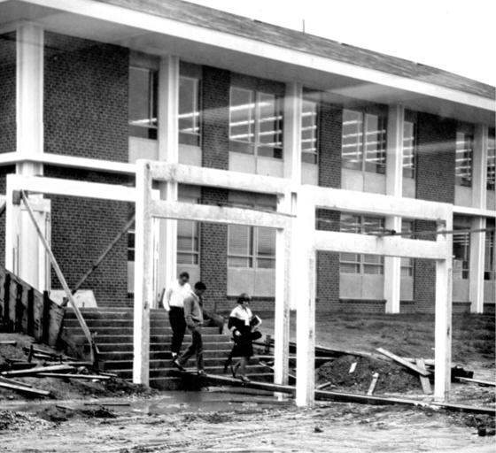 Students walk across a plank placed over a puddle between the East and South (today known as Krug) Buildings during the fall of 1964