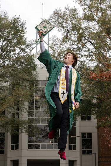 Cody Salenga, dressed in graduation robes, jumps in front of the Johnson Center.