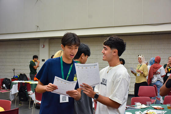 Two students with get-to-know-you bingo cards in hand talk