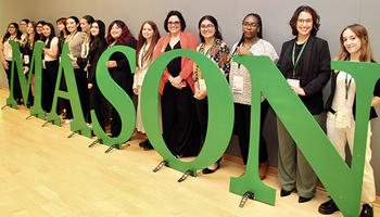 Several women stand behind very large letters spelling MASON.