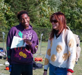 James Bah directing an actor on an outside film set with a smile.