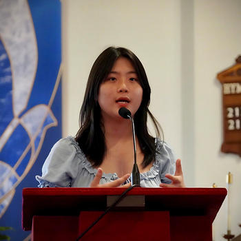 A woman with dark hair stands behind a brown lectern.